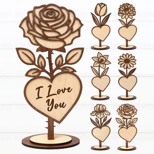 Op de afbeelding: Houten bloemdecoraties met hartvormige bases. Het hoofdgedeelte heeft een roos en de tekst "I Love You". Andere ontwerpen zijn een tulp, chrysant, narcis, madeliefje, iris en nog een roos. De stukken zijn gemaakt van licht en donkerbruin hout.
