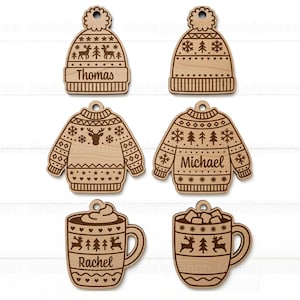 Puede incluir: Adornos navideños de madera con forma de gorro, suéter y tazas. Los adornos de gorro y suéter tienen nombres grabados. Las tazas están decoradas con renos y copos de nieve. Los adornos son de madera clara.