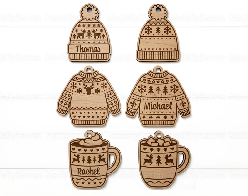 Op de afbeelding: Houten kerstversieringen in de vorm van een muts, trui en mokken. De muts- en truiornamenten zijn gegraveerd met namen. De mokken zijn versierd met rendieren en sneeuwvlokken. De ornamenten zijn gemaakt van lichtgekleurd hout.