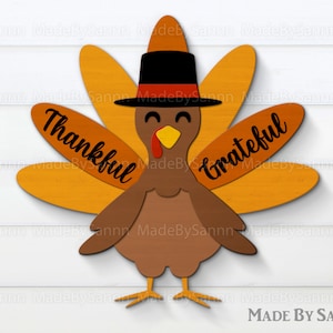 May include: A wooden turkey cutout decoration featuring a brown body, orange tail feathers, and a black top hat with a red band. The left feathers display the word Thankful in black script, and the right feathers display the word Grateful in black script.