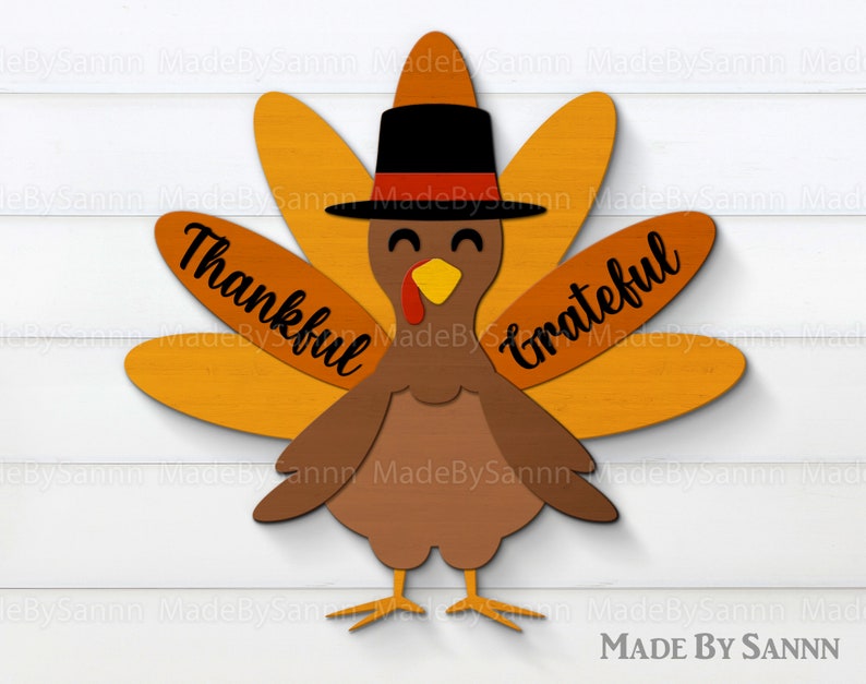 May include: A wooden turkey cutout decoration featuring a brown body, orange tail feathers, and a black top hat with a red band. The left feathers display the word Thankful in black script, and the right feathers display the word Grateful in black script.