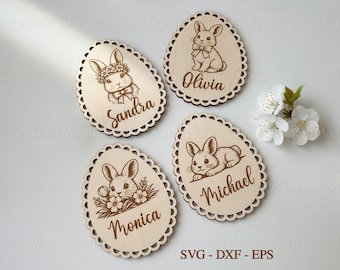 Puede incluir: Cuatro adornos de huevo de Pascua de madera con bordes festoneados. Cada huevo presenta un diseño de conejo cortado con láser y un nombre: Sandra, Olivia, Monica y Michael. Los adornos son de color marrón claro.