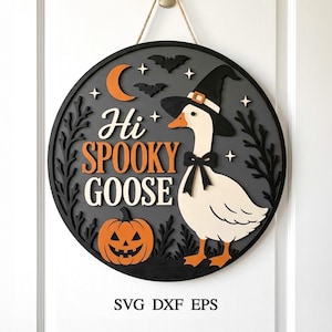 Puede incluir: Un letrero de pared circular de madera que presenta un ganso blanco con un sombrero de bruja negro y una pajarita. El letrero muestra el texto "Hi SPOOKY GOOSE" en naranja y blanco, acompañado de una calabaza naranja, murciélagos, estrellas y una luna creciente sobre un fondo gris oscuro. El texto "SVG DXF EPS" aparece debajo.