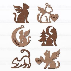 Op de afbeelding: Een verzameling van zes houten kattenornamenten in verschillende ontwerpen. Sommige katten hebben vleugels, zitten op een maan of houden een hart met de naam "Luna" vast. De ornamenten zijn gemaakt van bruin hout.