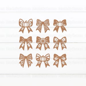 May include: Nine brown decorative bows with various fall-themed designs, including pumpkins, acorns, and leaves. The bows are arranged in three rows of three on a white wooden background. The bows are cut from a solid material.