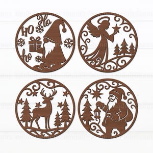 Puede incluir: Cuatro adornos navideños de madera con intrincados diseños recortados. Uno presenta un gnomo con la palabra "Ho" y copos de nieve. Otro muestra un ángel sosteniendo una estrella. También se representan un reno y Papá Noel.