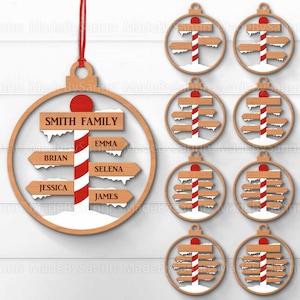 Può includere: Un set di nove ornamenti natalizi in legno a forma di segnale stradale con un palo di caramelle. Gli ornamenti hanno uno sfondo bianco con strisce di caramelle rosse e bianche. Gli ornamenti hanno nomi sui cartelli, tra cui "Smith Family", "Brian", "Emma", "Selena", "Jessica" e "James".