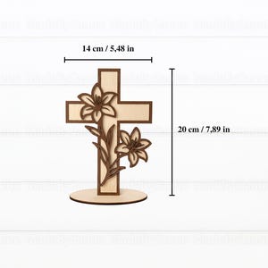 May include: A wooden cross with a lily flower design. The cross is 7.89 inches tall and 5.48 inches wide. The cross is made of light and dark brown wood and stands on a round base. The lilies are intricately carved.
