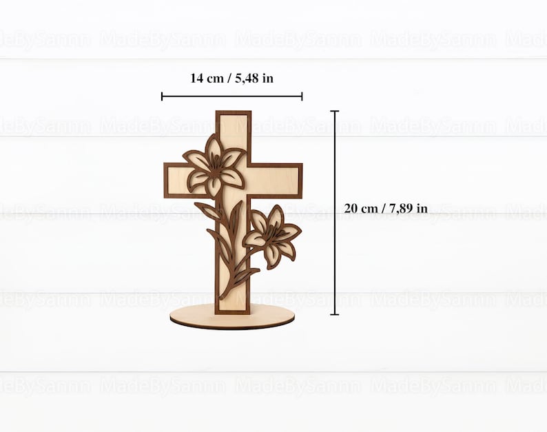 May include: A wooden cross with a lily flower design. The cross is 7.89 inches tall and 5.48 inches wide. The cross is made of light and dark brown wood and stands on a round base. The lilies are intricately carved.
