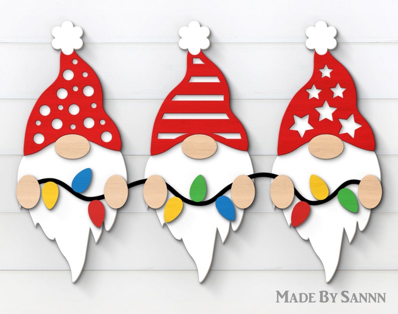 May include: Wooden Christmas gnome decorations with red hats featuring white polka dots, stripes, and stars. Each gnome has a wooden nose, white beard, and holds a string of colorful lights. The text "MADE BY SANNN" is visible.