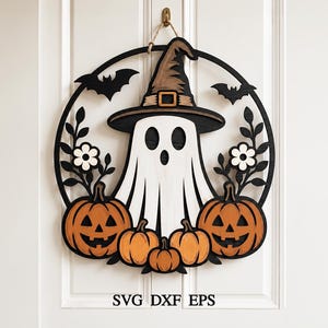 May include: A circular wooden wall hanging featuring a white ghost wearing a brown witch hat, surrounded by orange jack-o'-lantern pumpkins, black bats, and white flowers. The text SVG DXF EPS is printed at the bottom of the design.
