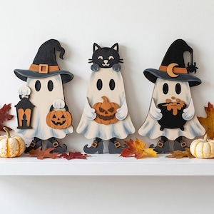 May include: Three wooden Halloween decorations featuring ghosts. The left ghost wears a black hat and holds a lantern and pumpkin. The center ghost has a black cat on its head and holds a pumpkin. The right ghost wears a hat with a moon and holds a cauldron.