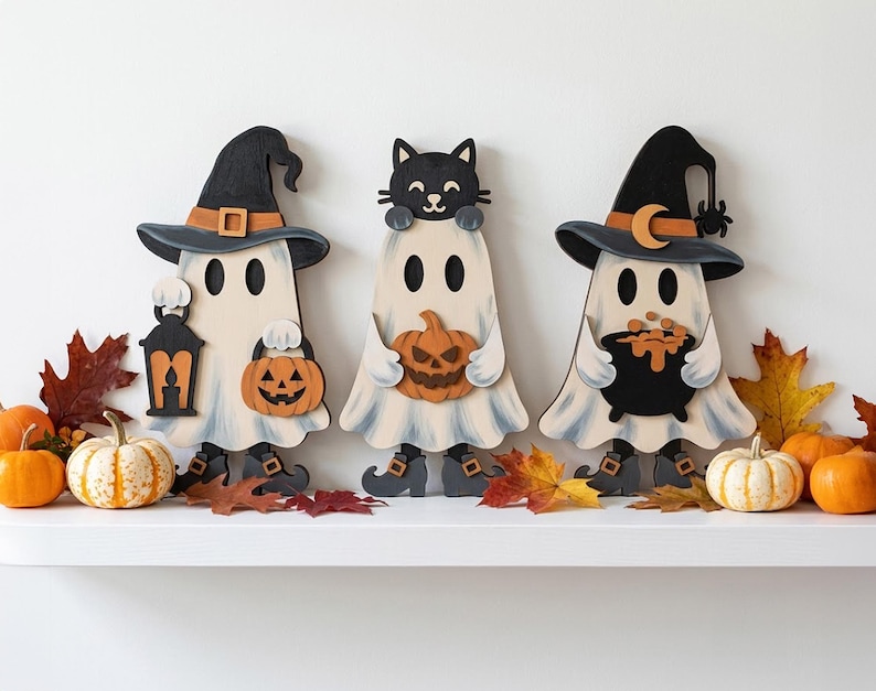 May include: Three wooden Halloween decorations featuring ghosts. The left ghost wears a black hat and holds a lantern and pumpkin. The center ghost has a black cat on its head and holds a pumpkin. The right ghost wears a hat with a moon and holds a cauldron.