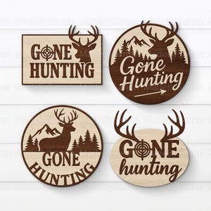 May include: Four wooden signs with a hunting theme. The signs feature deer antlers, the words "Gone Hunting," and a target symbol. Two signs are circular, one is rectangular, and one is oval-shaped. The signs are brown and beige.