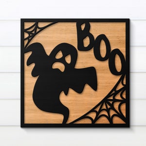 May include: A black wooden sign with a cutout of a ghost and the word "BOO" in a spooky font. The sign has a wood grain background and a black frame.