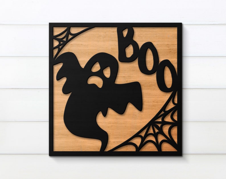 May include: A black wooden sign with a cutout of a ghost and the word "BOO" in a spooky font. The sign has a wood grain background and a black frame.