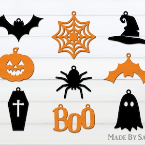 Puede incluir: Nueve adornos de madera con temática de Halloween en negro y naranja. Los adornos incluyen un murciélago, una araña, un fantasma, una calabaza, un ataúd, un sombrero de bruja, una telaraña, alas de murciélago y la palabra "Boo".