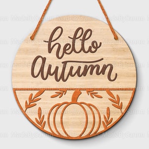 May include: A round wooden sign with the text "hello autumn" in brown lettering. The bottom half of the sign features a stylized pumpkin with leaves.