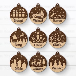 Pode incluir: Nove enfeites de Natal de madeira com vários desenhos e nomes. Os enfeites apresentam imagens cortadas a laser de presentes, um caminhão, uma casa, o trenó do Papai Noel, velas, bengalas doces, uma igreja, veados e árvores.