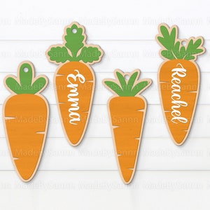 May include: Four orange carrot-shaped wooden ornaments with green tops. The carrots have the names "Emma" and "Reachel" written on them.