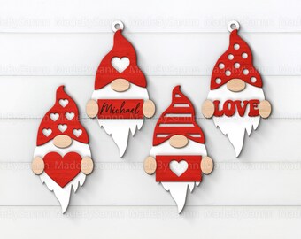 Puede incluir: Cuatro adornos de gnomos de madera con sombreros rojos y barbas blancas. Un gnomo tiene la palabra "LOVE", otro el nombre "Michael", y los demás tienen diseños de corazón. Cada uno tiene una nariz de madera y un pequeño lazo para colgar.