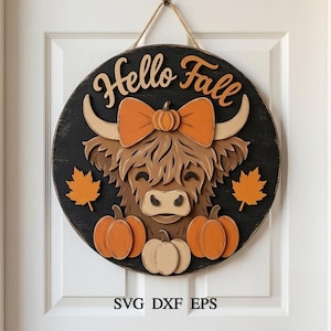 May include: A circular wooden wall sign with a black background featuring a layered cutout of a brown Highland cow wearing an orange bow. The text Hello Fall is at the top, with orange maple leaves and three pumpkins below. It hangs by a rope.