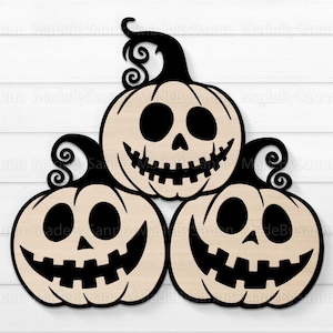 May include: Three black and white carved wooden pumpkins with jack-o'-lantern faces. The pumpkins are stacked on top of each other.