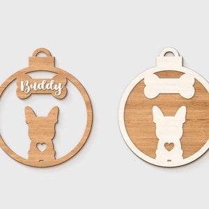 Pu&ograve; includere: Un ornamento natalizio in legno a forma di palla con una silhouette bianca di un cane e un osso con la parola "Buddy" su di esso.