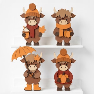 May include: Four layered wooden cutouts of Highland cattle figures in autumn-themed attire. One wears a beanie and scarf holding a coffee cup and leaf, another a scarf holding a pumpkin, one with an umbrella and boots, and one in a sweater holding a pumpkin.