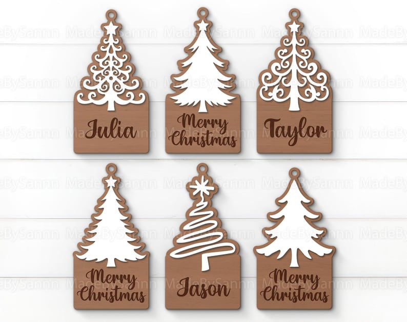 Peut inclure: Six d&eacute;corations de No&euml;l en bois brun avec des arbres d&eacute;coup&eacute;s en blanc. Les d&eacute;corations portent les noms "Julia", "Joyeux No&euml;l", "Taylor", "Joyeux No&euml;l", "Jason" et "Joyeux No&euml;l".