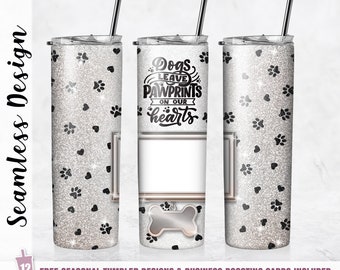 May include: A white tumbler with a silver glitter finish and black paw prints and hearts. The tumbler has a white insert with the text "Dogs leave pawprints on our hearts".