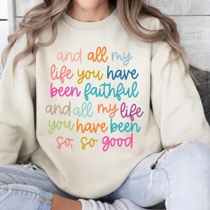 May include: Cream-colored sweatshirt with the text "and all my life you have been faithful and all my life you have been so, so good" in colorful lettering. The sweatshirt is a casual, comfortable style.
