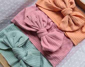 May include: Three fabric headbands with large bows. The headbands are in shades of peach, pink, and teal.