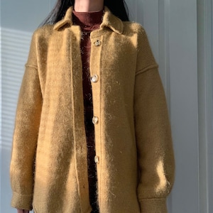 May include: A mustard yellow knitted cardigan with a button-up front and long sleeves. The cardigan has a relaxed fit and a slightly oversized silhouette.