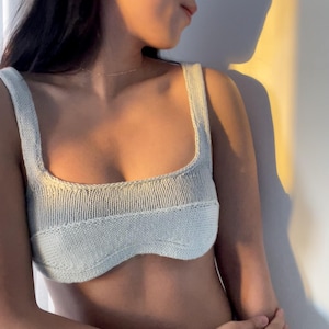 May include: A light blue knitted crop top with a scoop neck and a curved bottom.