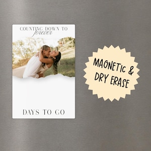 May include: A rectangular magnetic dry erase board featuring a photograph of a couple embracing at the top, with the text "COUNTING DOWN TO forever" above the image and "DAYS TO GO" at the bottom. A starburst graphic reads "MAGNETIC & DRY ERASE".