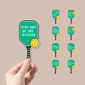 May include: Nine green and black pickleball paddle stickers with various pickleball-themed sayings. The sayings include "Great Minds Dink Alike", "Life is Short Play Pickleball", "Stay Out of the Kitchen", "I Have a Dinking Problem", "Let's Get Pickled", "Dinking All Day", "Eat Sleep Pickleball Repeat", "I'll Dink to That", and "Sorry, I Can't Dink Today".