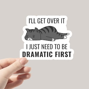 May include: A white sticker with a black and white illustration of a cat lying down. The text on the sticker reads "I'll get over it, I just need to be dramatic first."