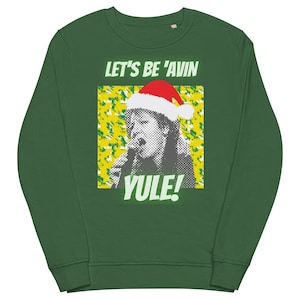Può includere: Una felpa verde scuro con la scritta bianca "LET'S BE 'AVIN YULE!". Il design presenta una grafica di una persona con un cappello di Babbo Natale, su uno sfondo giallo e verde. Un capo festivo a tema natalizio.