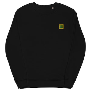 Peut inclure: Sweat-shirt noir à col rond avec un petit écusson brodé portant le numéro "10" dans un carré doré avec une bordure verte. Le sweat-shirt est fait d'une matière douce.