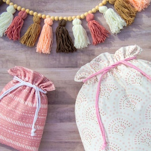 Puede incluir: Dos bolsas de tela con cord&oacute;n de ajuste. Una bolsa es rosa con lunares blancos y la otra es blanca con lunares rosas y marrones. Ambas bolsas tienen cordones de ajuste rosas.