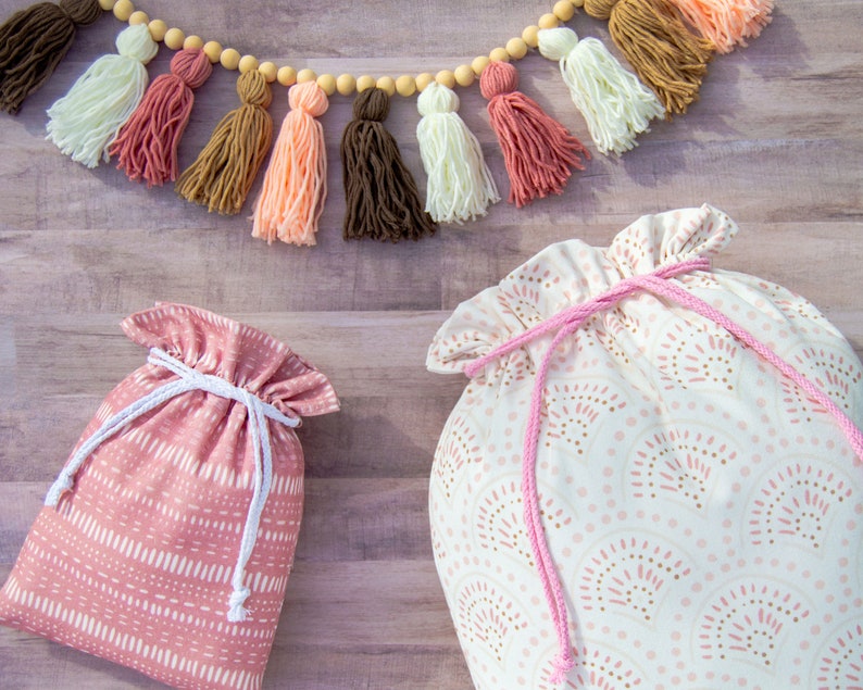 Puede incluir: Dos bolsas de tela con cord&oacute;n de ajuste. Una bolsa es rosa con lunares blancos y la otra es blanca con lunares rosas y marrones. Ambas bolsas tienen cordones de ajuste rosas.