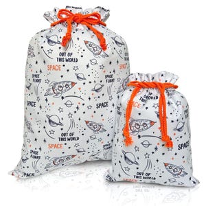 May include: Two white drawstring bags with an outer space theme. The bags feature a repeating pattern of rockets, planets, and stars in black and orange. Text on the bags reads "OUT OF THIS WORLD" and "SPACE". The drawstrings are bright orange.