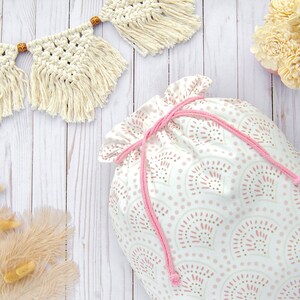 Puede incluir: Una bolsa de cord&oacute;n blanco con un patr&oacute;n geom&eacute;trico rosa y blanco. La bolsa est&aacute; hecha de tela y tiene un cord&oacute;n rosa.