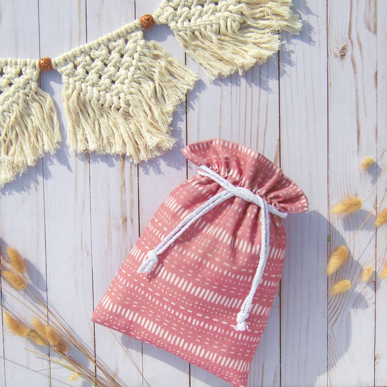 Puede incluir: Una bolsa de cord&oacute;n rosa con un cord&oacute;n blanco y un patr&oacute;n geom&eacute;trico blanco y rosa. La bolsa est&aacute; sobre una superficie de madera blanca.