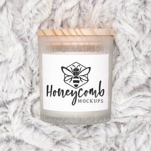 May include: A frosted glass candle jar with a wooden lid and a white label. The label has a black and white illustration of a bee in a honeycomb and the text "Honeycomb Mockups".