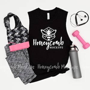 May include: A black sleeveless workout shirt with the text "Honeycomb Mockups" and a bee logo, paired with gray leggings, a pink dumbbell, a gray water bottle, and black wireless earbuds. A pink headband is also included.