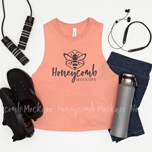 May include: A flat lay of fitness accessories including a coral tank top with a bee logo and the text "Honeycomb Mockups", black running shoes, a water bottle, a pair of black wireless headphones, and a jump rope.