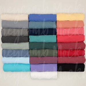 Op de afbeelding: Een stapel gevouwen T-shirts in verschillende kleuren, waaronder wit, lichtblauw, geel, rood en groen.