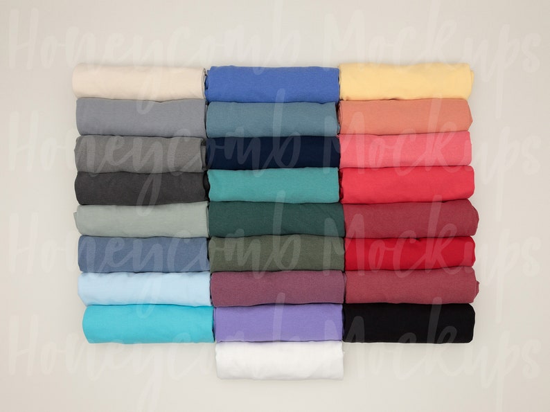 Op de afbeelding: Een stapel gevouwen T-shirts in verschillende kleuren, waaronder wit, lichtblauw, geel, rood en groen.